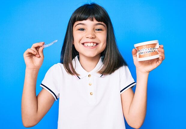 Giovane bambina sorridente tiene in mano un apparecchio ortodontico tradizionale e un apparecchio ortodontico